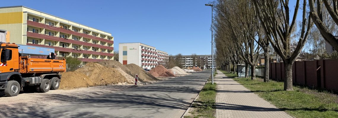 Entlang der Straße sind große Haufen Erdaushub aufgeschüttet. Rechts ist eine geklinkerte Sichtschutzwand für die Anwohner und Anwohnerinnen. entstanden.